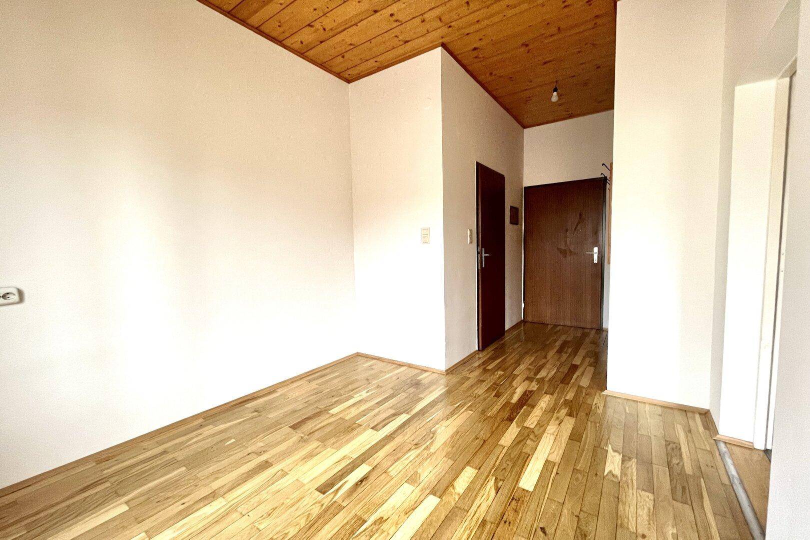Geräumiger Flur mit Holzbalkendecke, Parkettboden und zwei dunklen Türen, die zu weiteren Räumen führen.