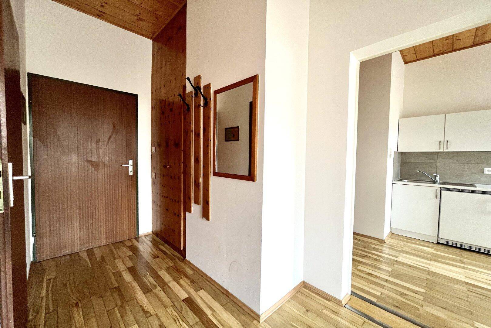 Eingangsbereich mit Holzbalkendecke, Parkettboden und einem Spiegel, der zum Küchenbereich führt.