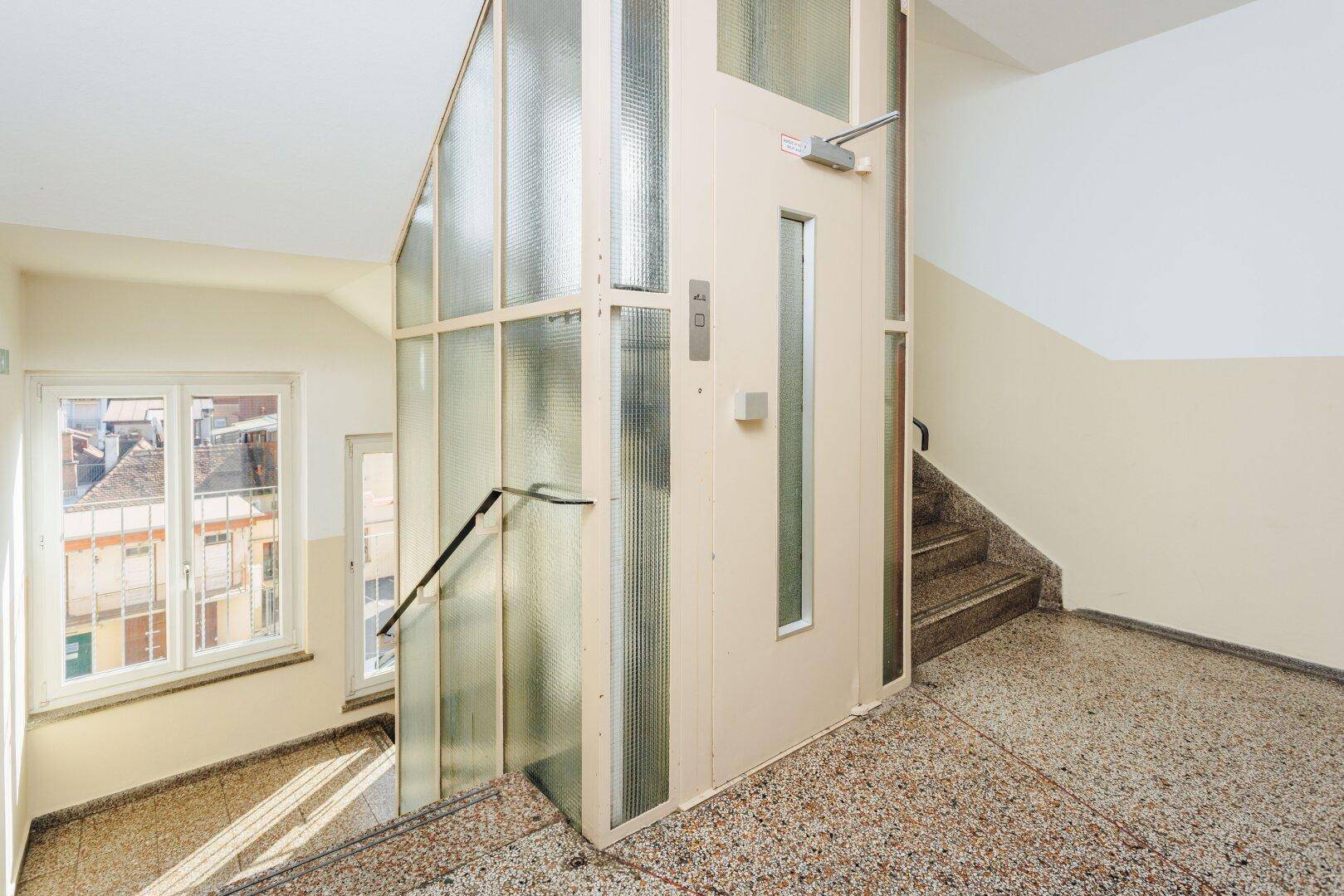 Treppenhaus mit Aufzug und Terrazzoboden in einem Mehrfamilienhaus.