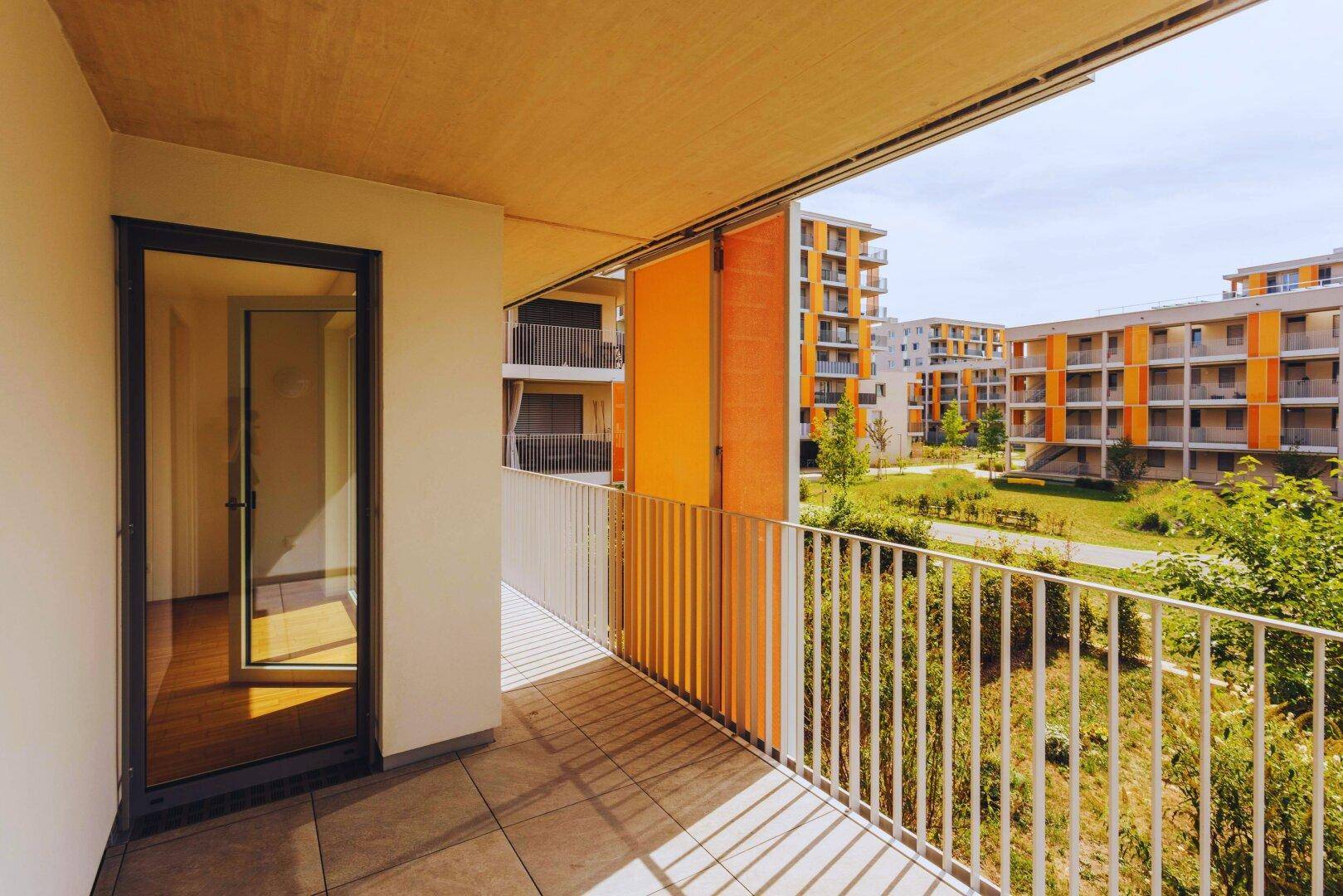 Geräumiger Balkon mit Fliesenboden und Metallgeländer, bietet Blick auf moderne Wohngebäude und Grünflächen.