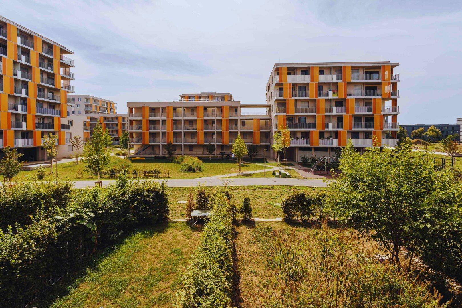 Moderne Wohnanlage mit mehreren Gebäuden, großzügigen Grünflächen und Wegen im Freien.