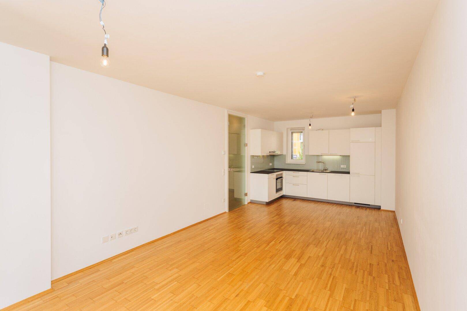 Offener Wohnbereich mit Holzboden und integrierter moderner Küche in Weiß, ideal für geselliges Beisammensein.