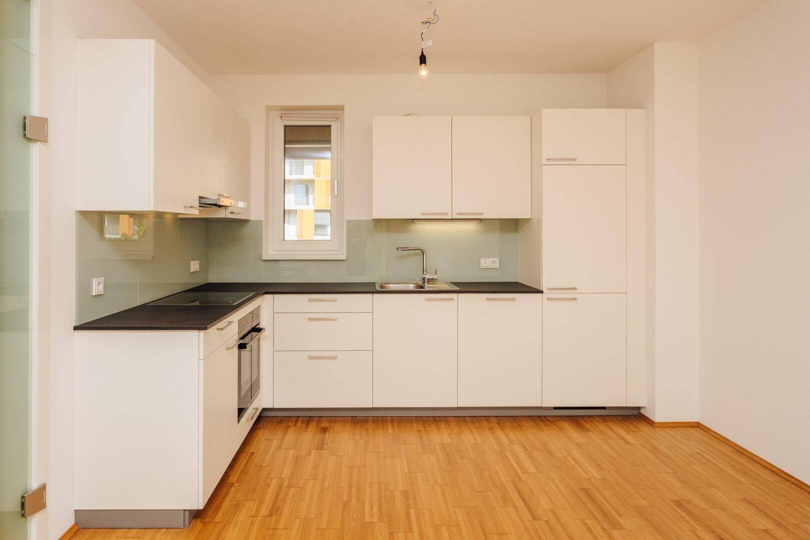 Moderne weiße Einbauküche mit dunklen Arbeitsplatten und Fenster, ausgestattet mit grundlegenden Geräten.