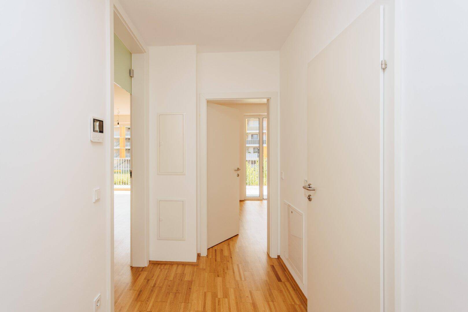 Heller Flur mit Holzboden und weißen Wänden, der zu verschiedenen Räumen der Wohnung führt.