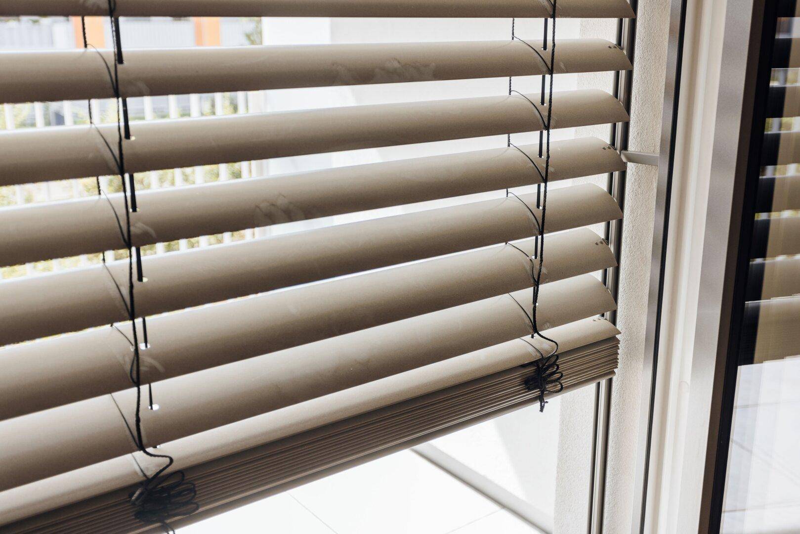Nahaufnahme von horizontalen Jalousien an einem Fenster, die das Tageslicht effektiv regulieren.