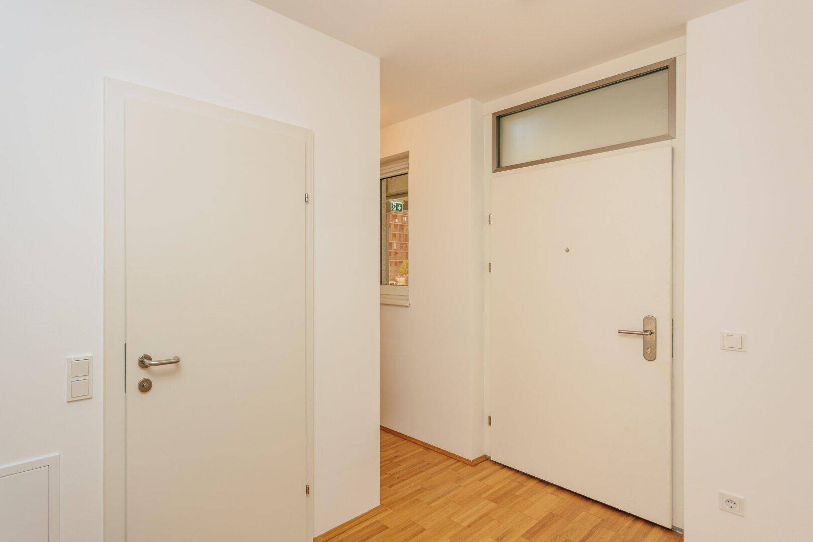 Eingangsbereich mit weißer Eingangstür und Innentür, ausgestattet mit Holzboden und hellen Wänden.