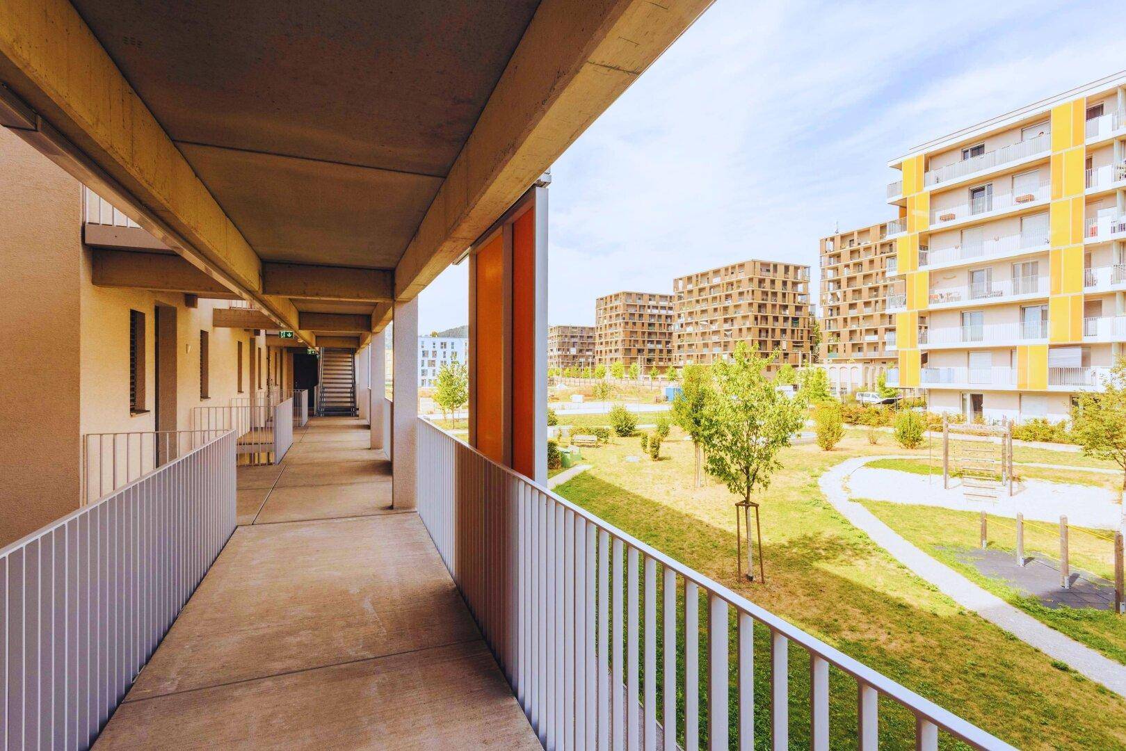 Außenflur eines Wohngebäudes mit Blick auf Grünflächen und weitere Gebäude der modernen Anlage.