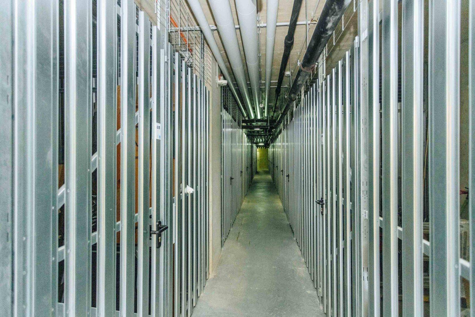 Reihen von Lagereinheiten mit Metallgittern in einem Keller oder Abstellraum, bieten viel Stauraum.