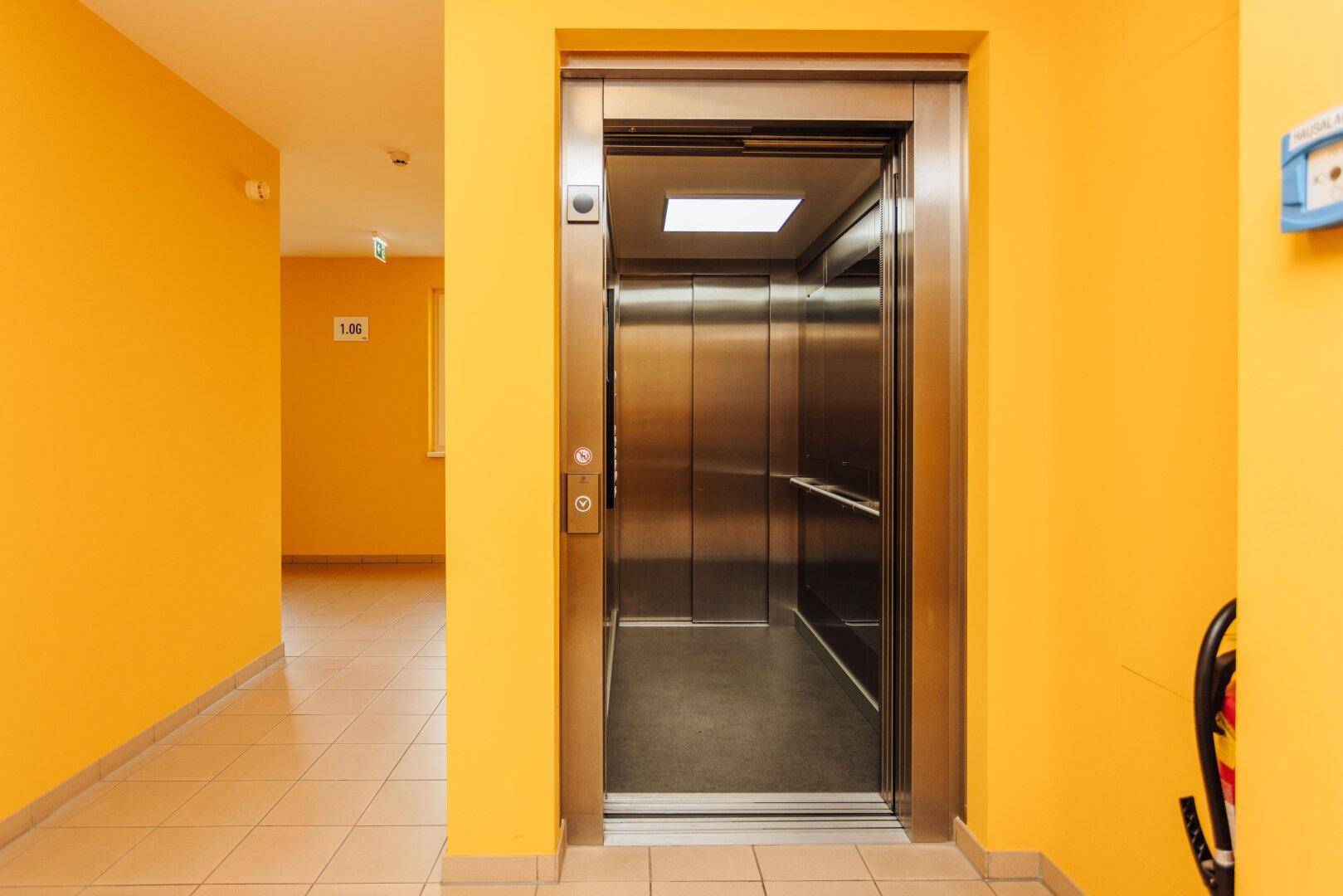 Moderner Aufzug in einem Gebäude mit leuchtend gelben Wänden im Flurbereich, gut zugänglich.