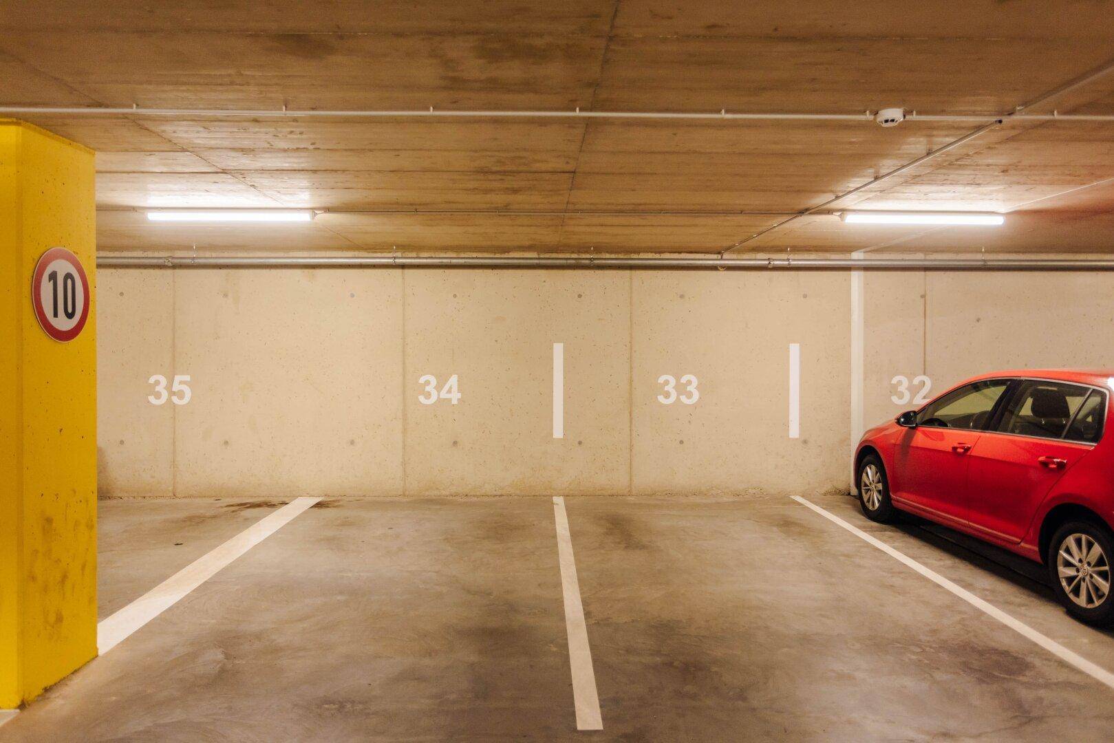 Tiefgarage mit nummerierten Stellplätzen und heller Beleuchtung, ein rotes Auto parkt.