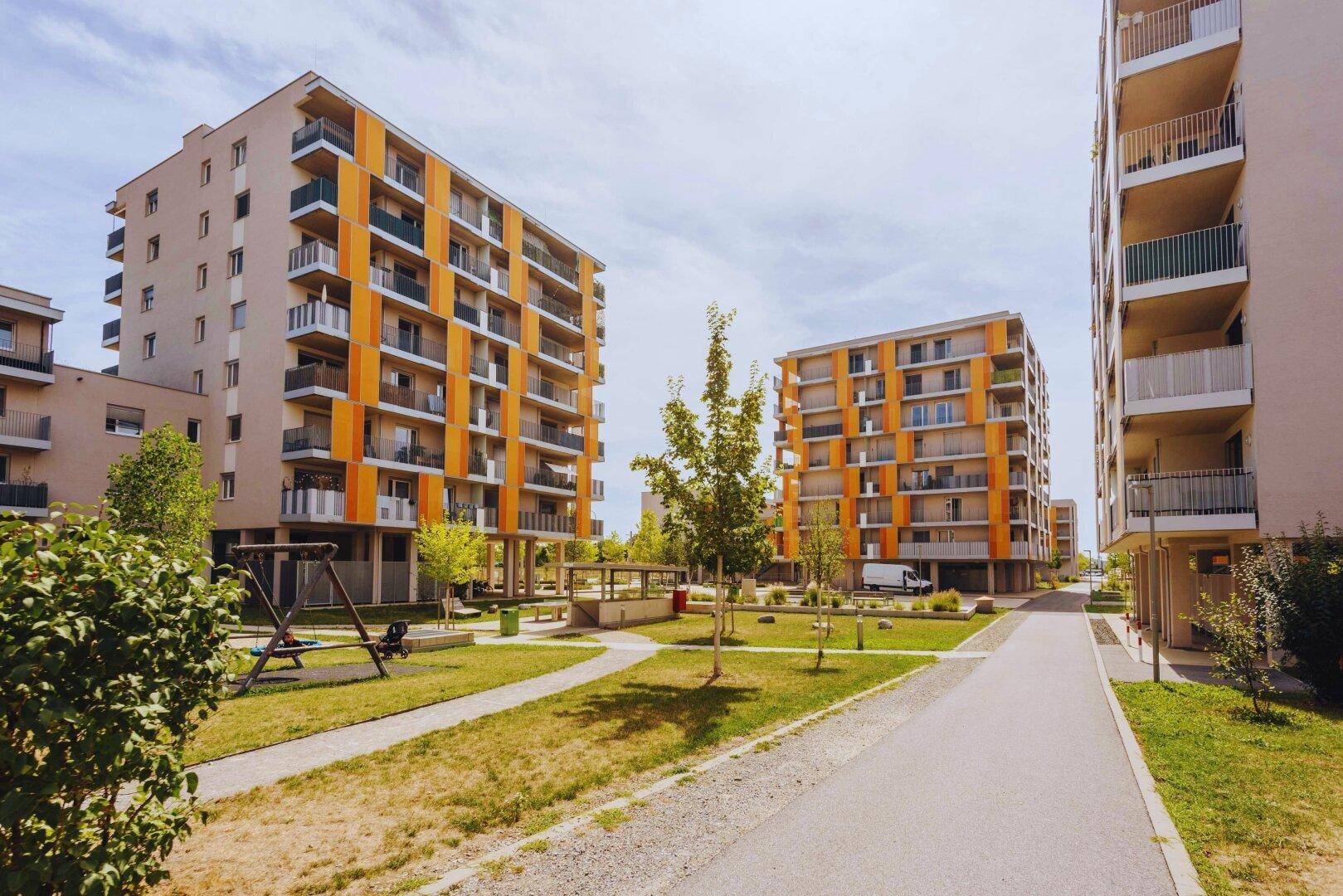 Moderne Wohngebäude mit orangefarbenen Akzenten und Grünflächen mit Spielplatz.