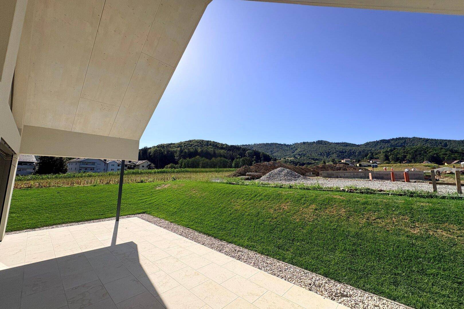 Weitläufiger Blick von der überdachten Terrasse über den grünen Garten und die umliegende Hügellandschaft.