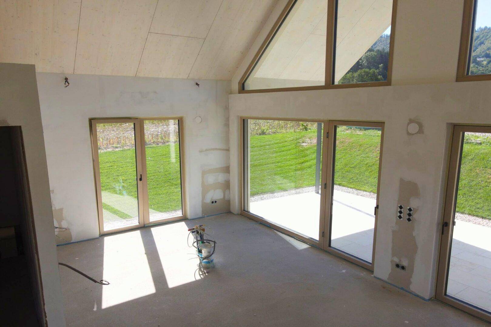 Lichtdurchfluteter Rohbau mit hohen Giebelfenstern und direktem Zugang zur zukünftigen Terrasse.