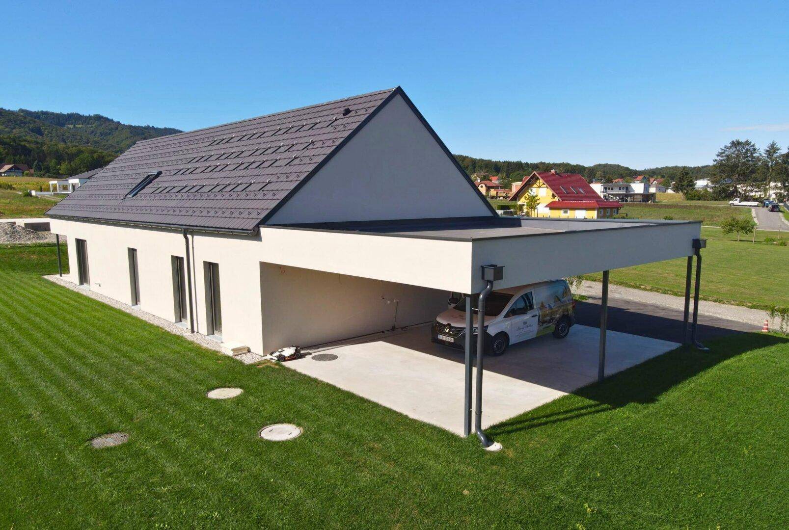 Modernes Einfamilienhaus mit großem Carport und Flachdach, umgeben von einer weitläufigen Grünfläche.