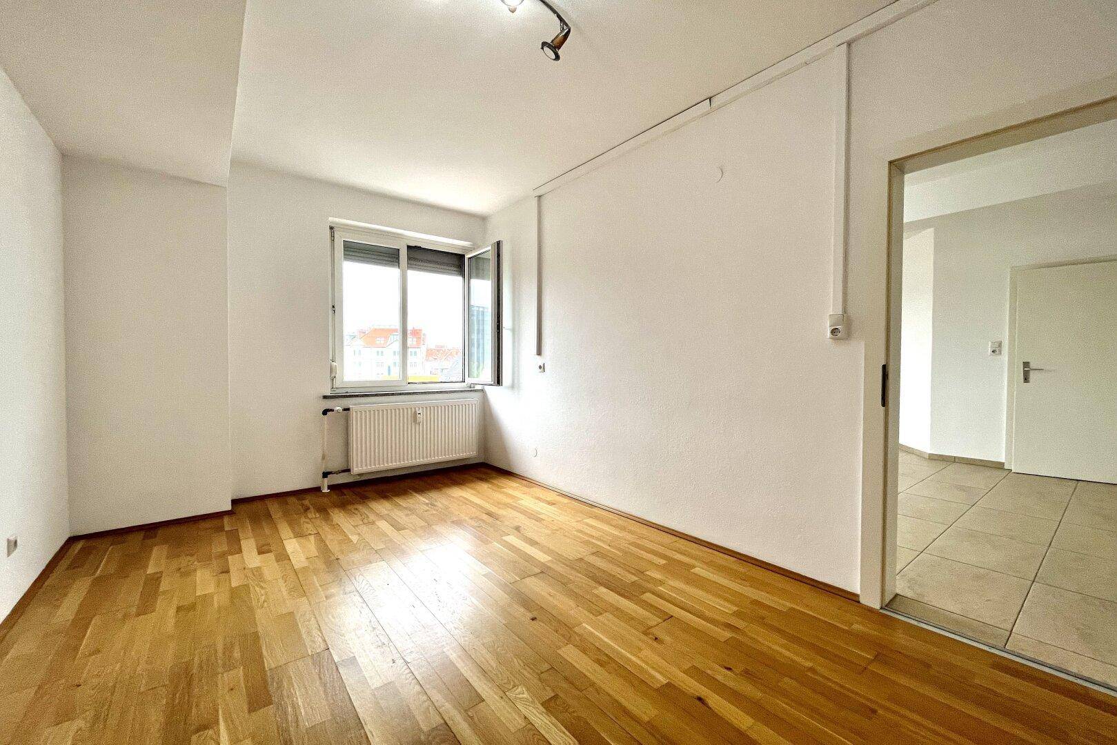 Heller Raum mit Holzparkettboden und einem Fenster mit Rollladen.