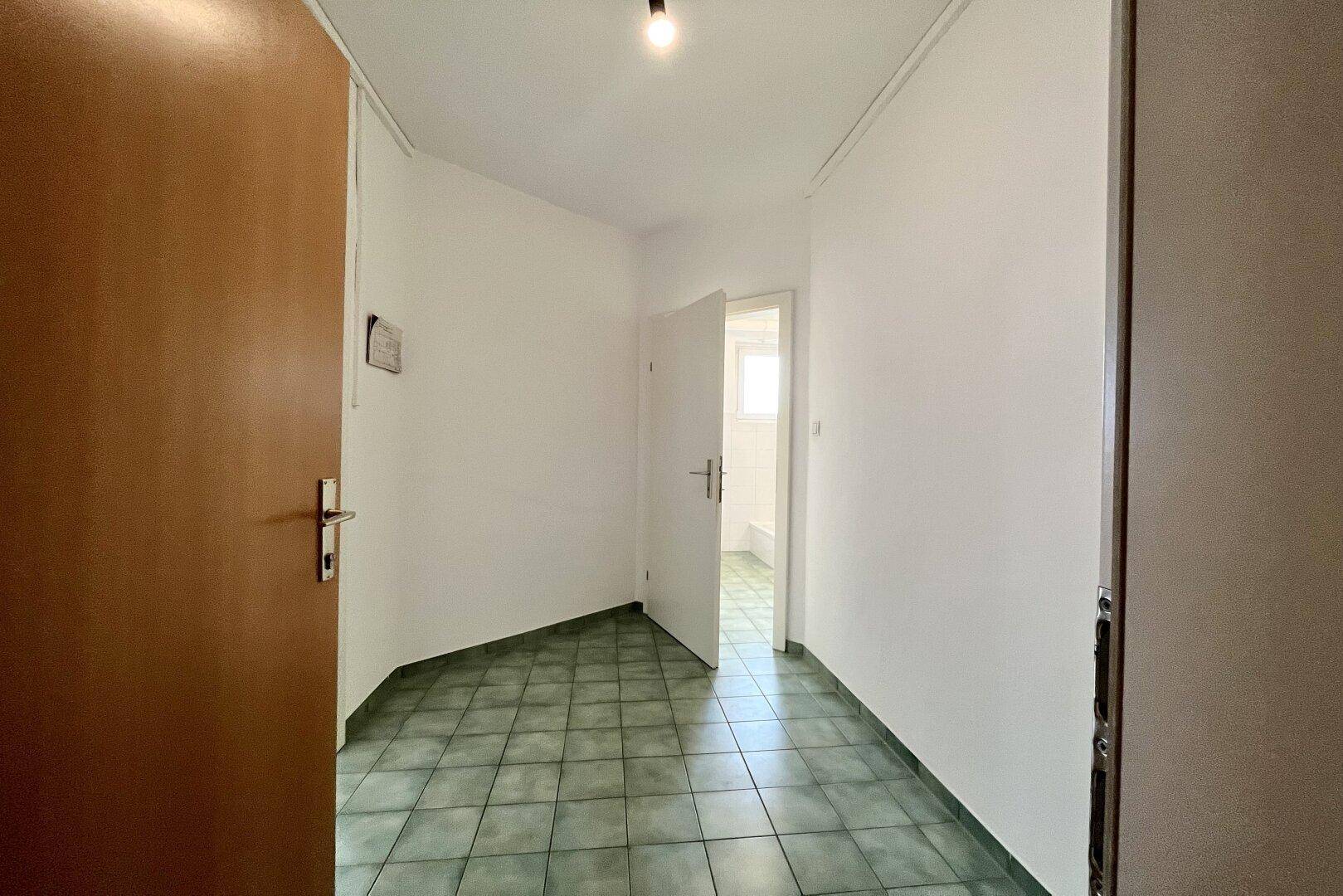 Flur mit grünem Fliesenboden und Zugang zu einem Badezimmer mit Tageslicht.