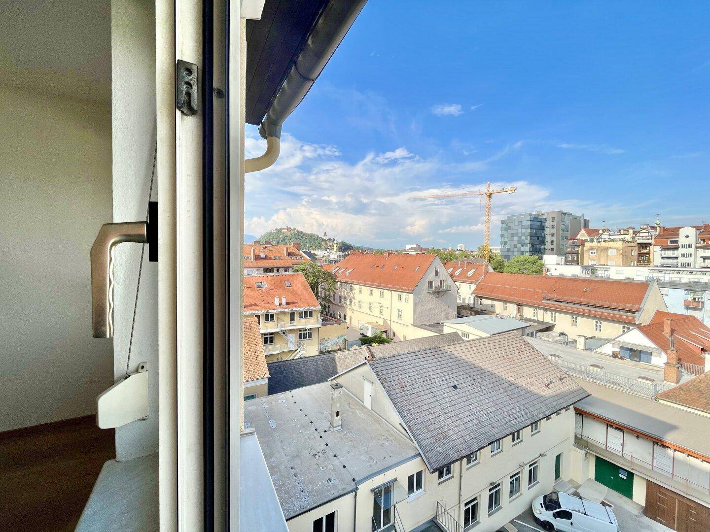 Blick aus dem Fenster auf eine städtische Umgebung mit Dächern und einem Kran.