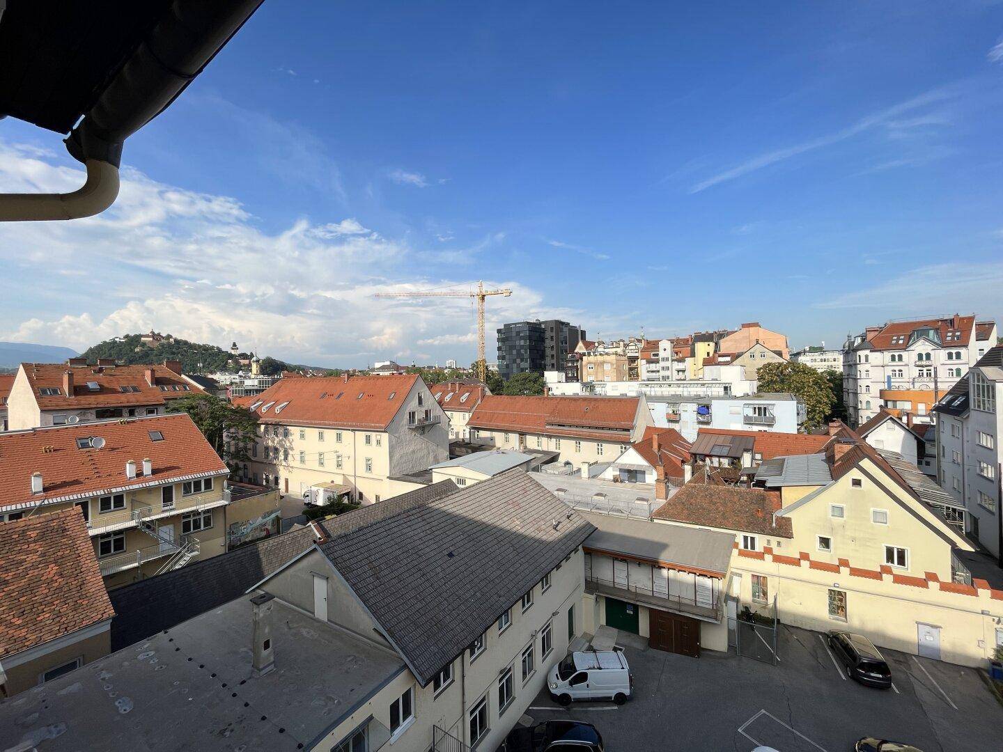 Weitläufiger Blick über die Dächer einer Stadt mit Bergen im Hintergrund.