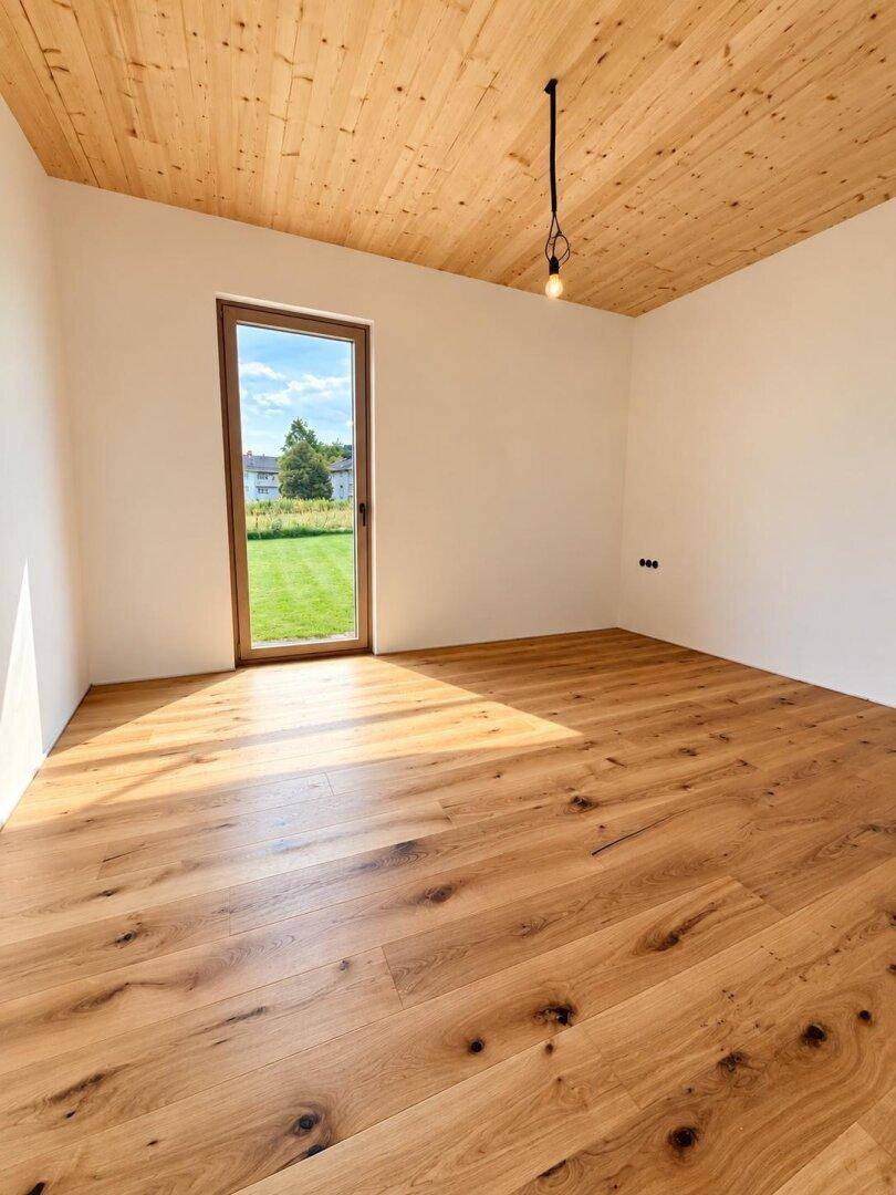 Helles Schlafzimmer mit Holzboden und einer Tür, die ins Grüne führt.