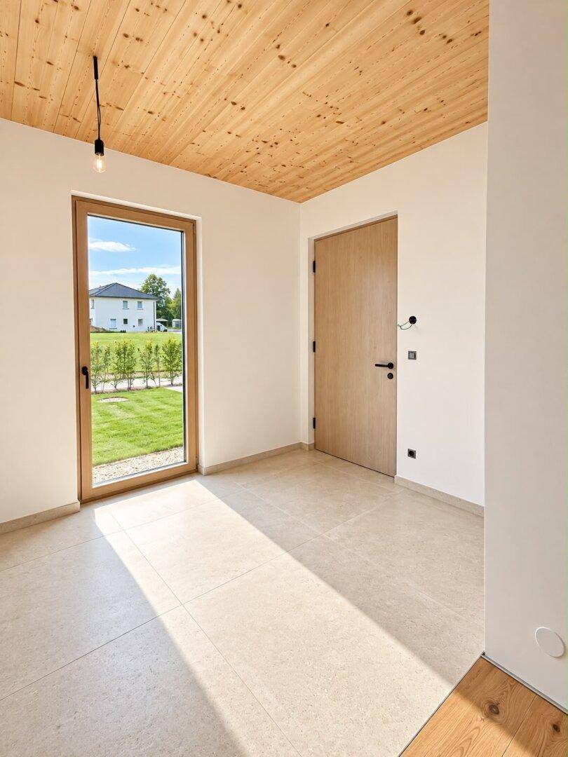 Heller Raum mit Fliesenboden und Zugang zu einem Gartenbereich mit Blick auf Nachbarhäuser.