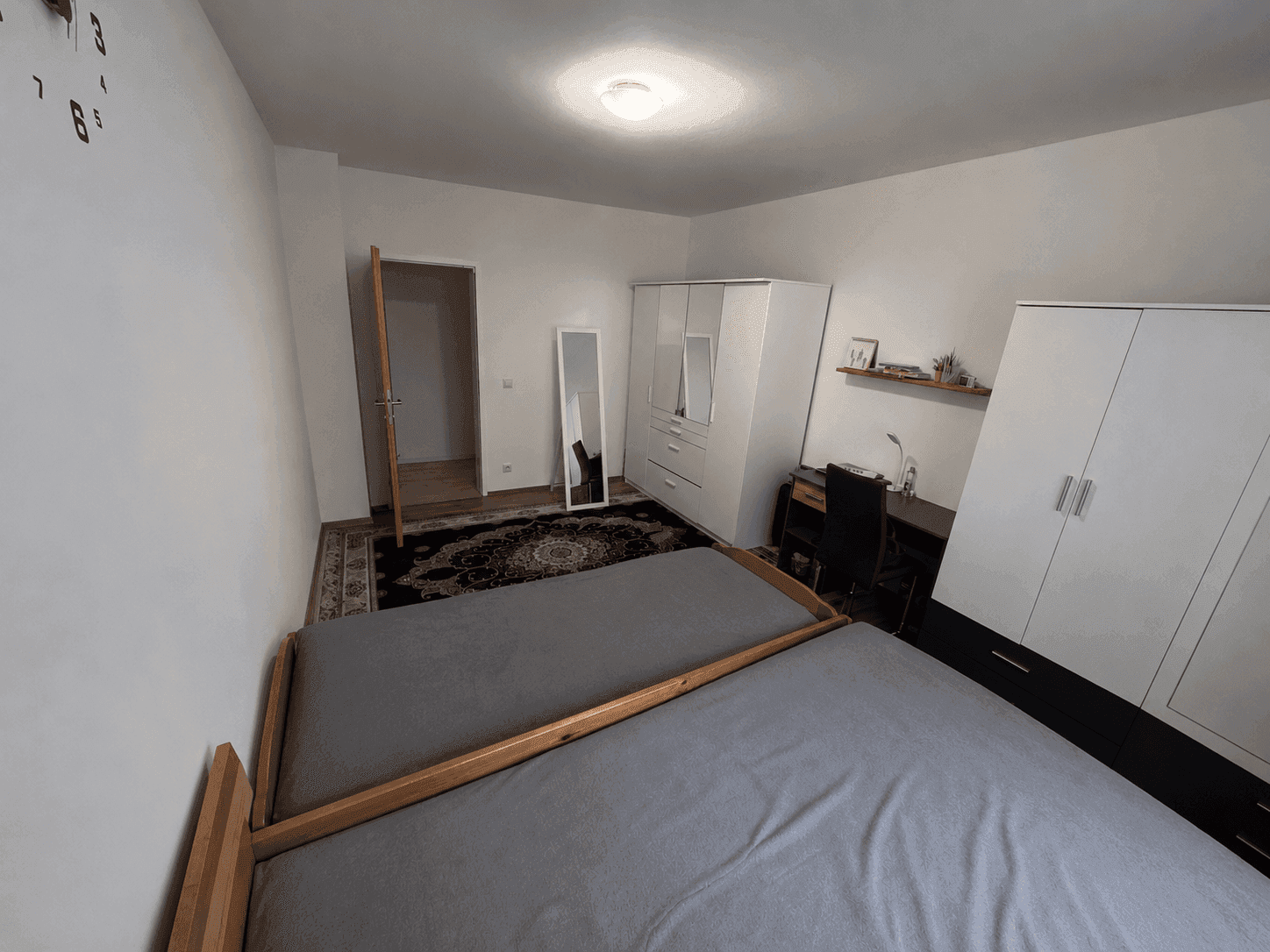Helles Schlafzimmer mit zwei Einzelbetten, weißen Kleiderschränken und einem Schreibtischbereich.