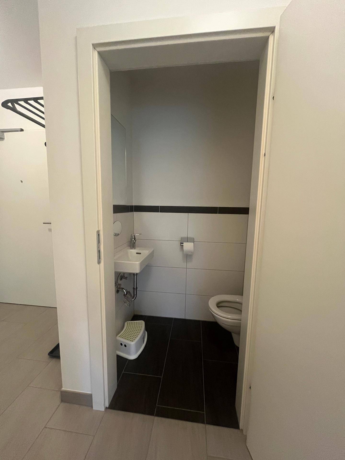 Kleines Gäste-WC mit Toilette, Handwaschbecken und dunklen Bodenfliesen.