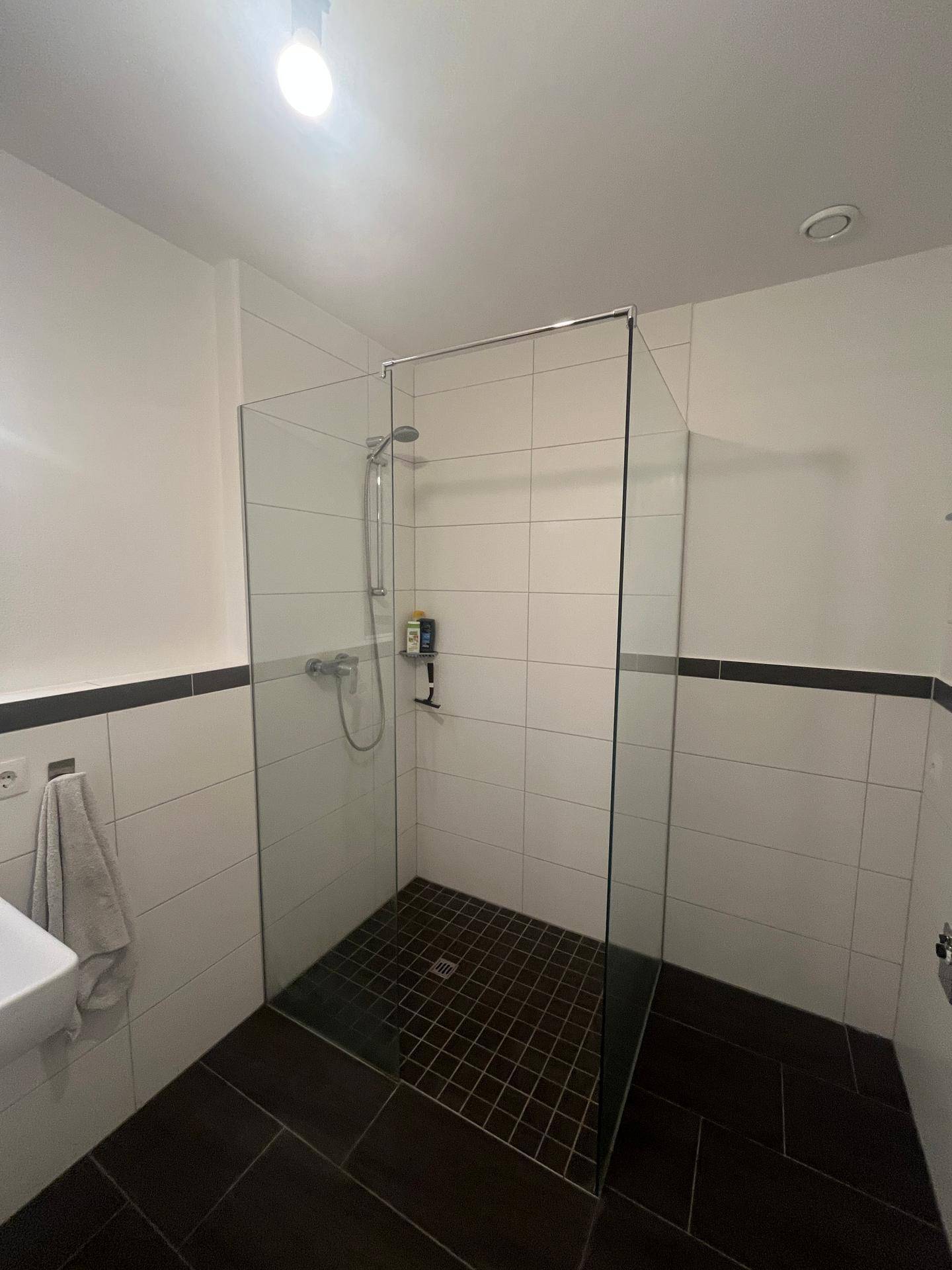Geräumige begehbare Dusche mit Glasabtrennung und dunklem Fliesenboden im Badezimmer.