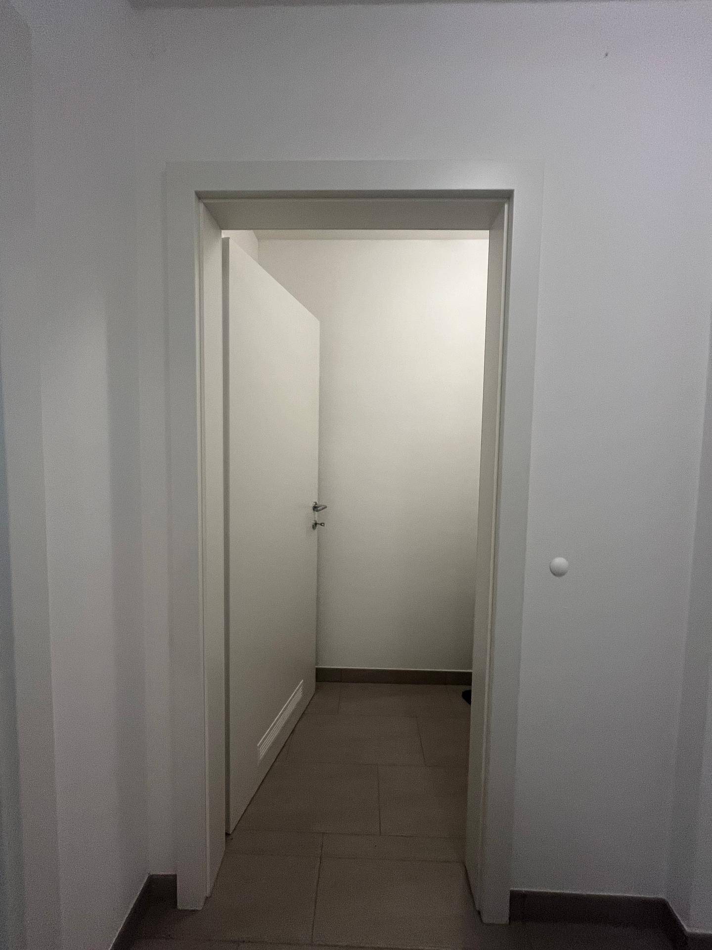 Heller Flur mit Fliesenboden und einer offenen Tür zu einem weiteren Raum.