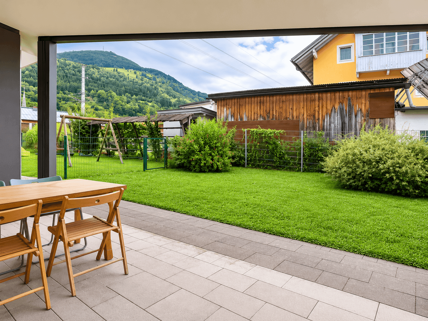 Geräumige Terrasse mit Esstisch und Blick auf den grünen Garten und die umliegenden Berge.