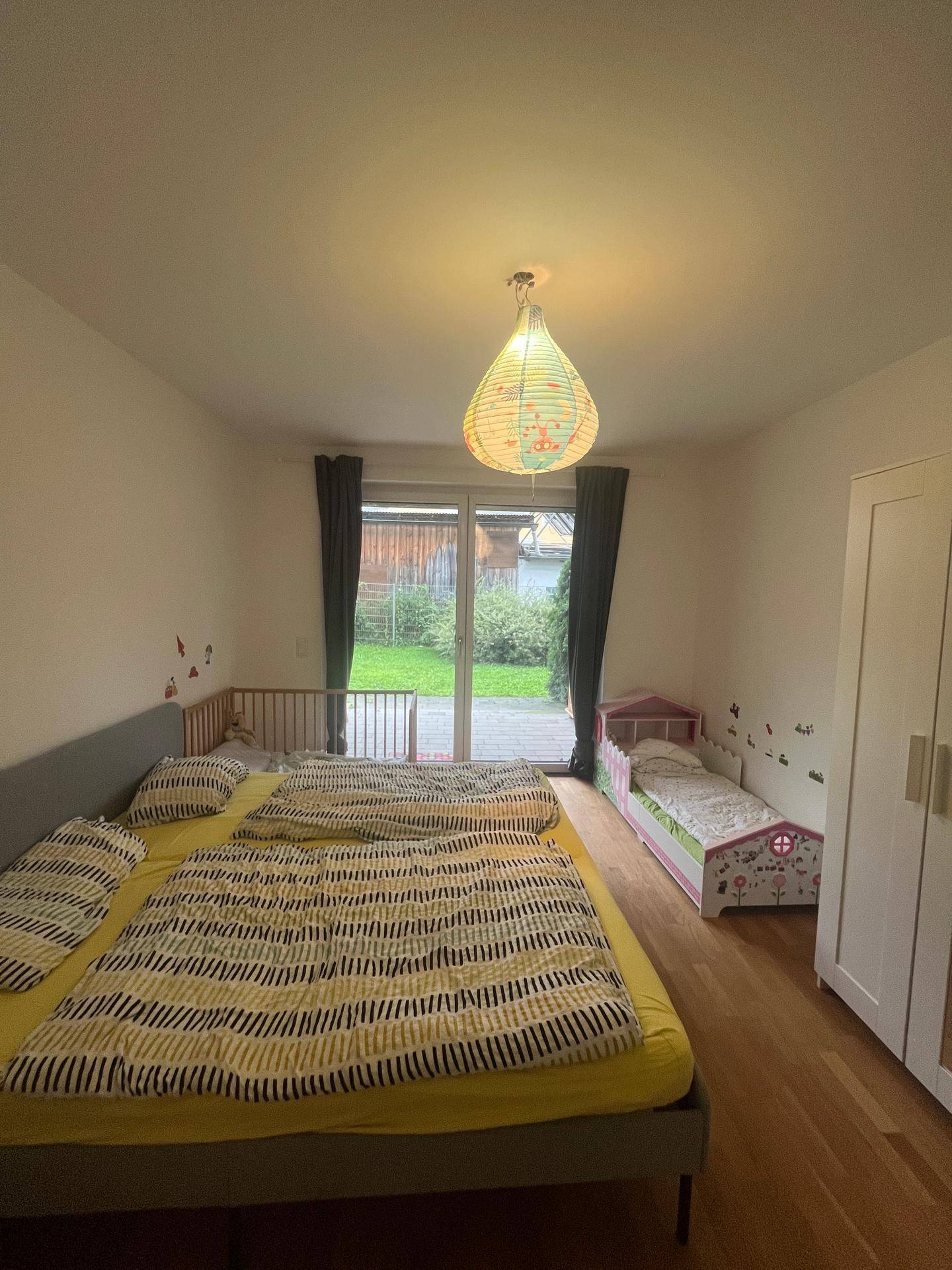 Helles Schlafzimmer mit Doppelbett, Kinderbetten und Zugang zum Garten.