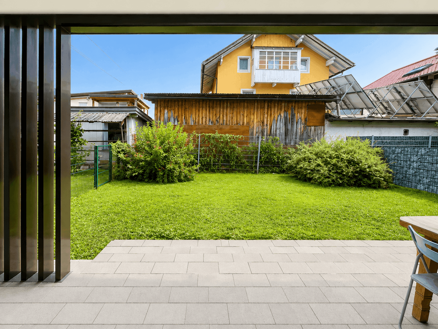 Blick von der Terrasse auf einen grünen Rasen und ein charmantes Holzhaus im Hintergrund.
