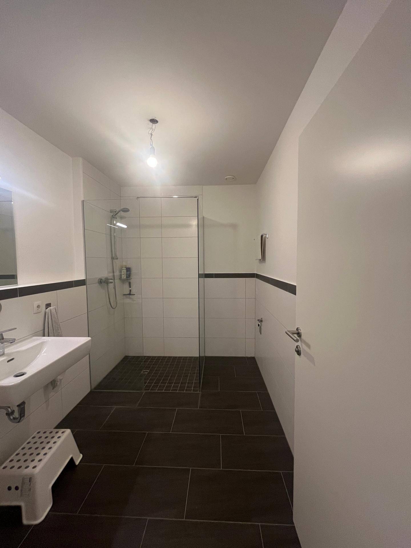 Modernes Badezimmer mit großer begehbarer Dusche, Einzelwaschbecken und dunklen Bodenfliesen.