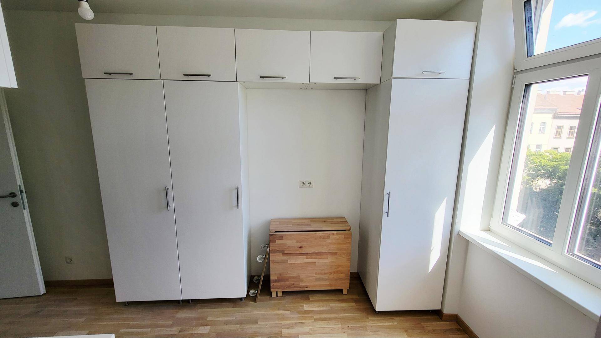 Schlafzimmer mit weißen Einbauschränken, Holzfußboden und großem Fenster für viel Tageslicht.