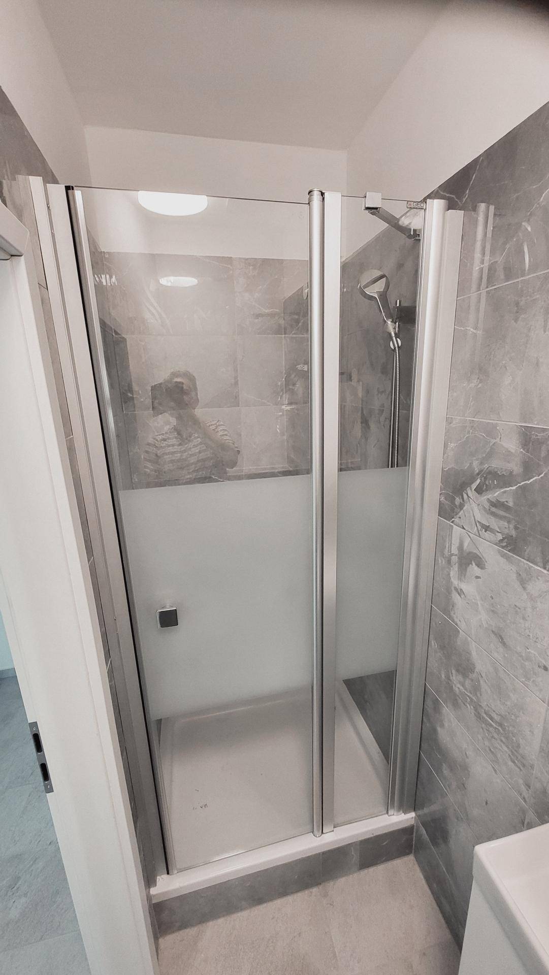 Duschkabine mit Glaswänden und moderner Armatur in einem gefliesten Badezimmer.