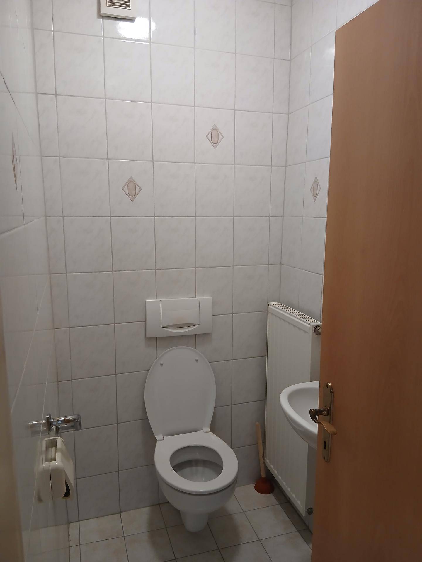 Kleines Gäste-WC mit WC, Waschbecken und hellen Fliesen an Wänden und Boden.