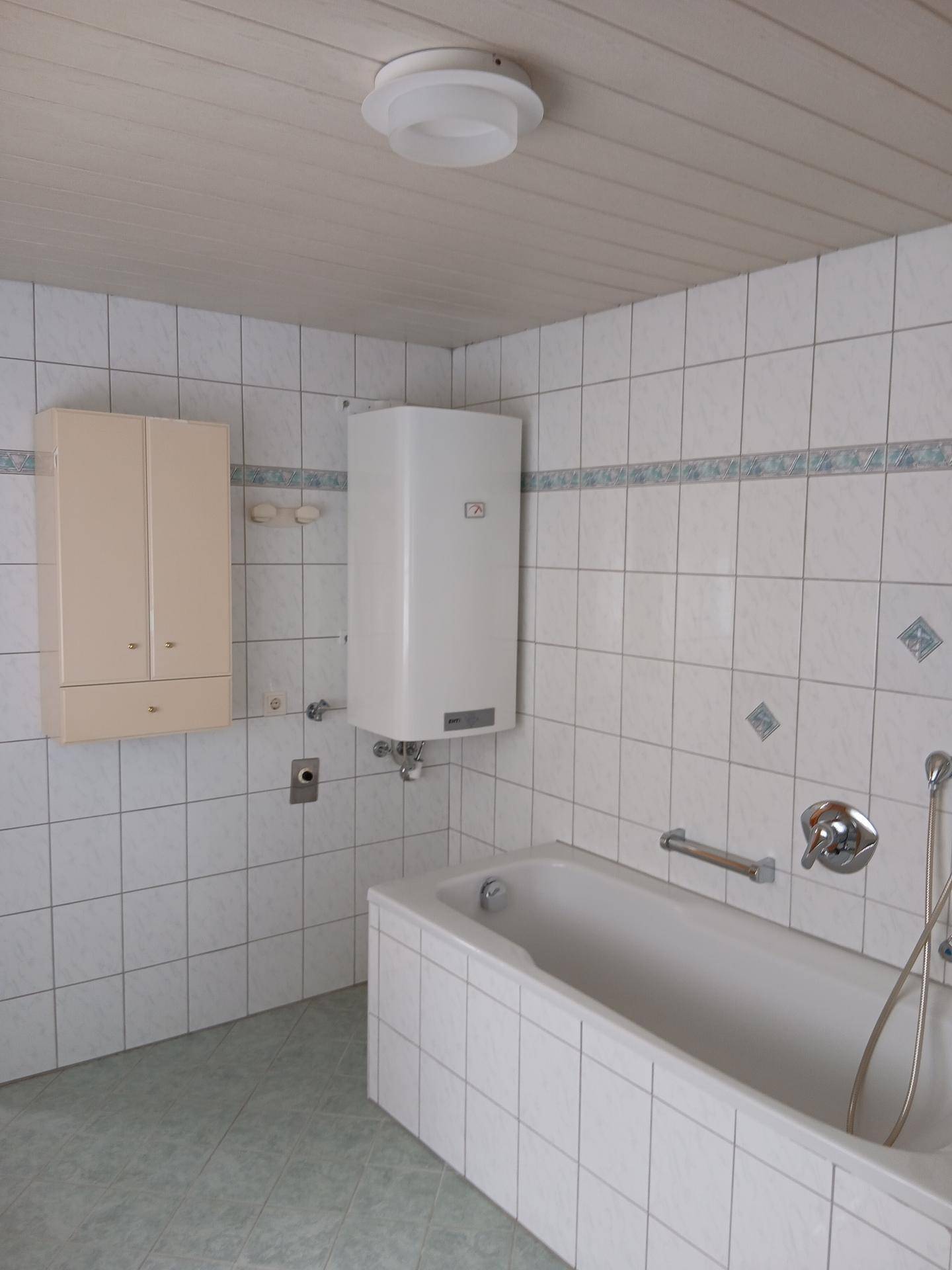 Badewanne und Warmwasserbereiter im Badezimmer mit weißen Fliesen.