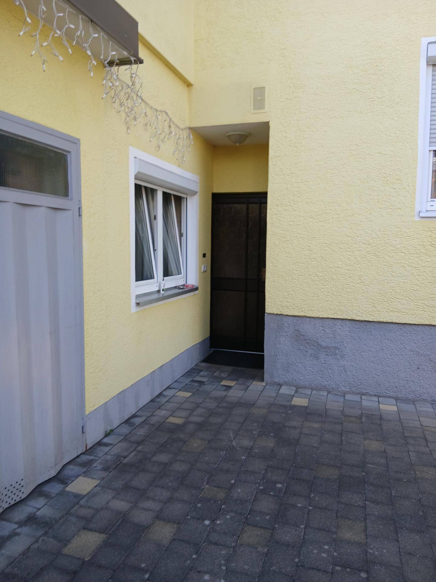 Eingangsbereich des Hauses mit gepflastertem Vorplatz und Haustür.