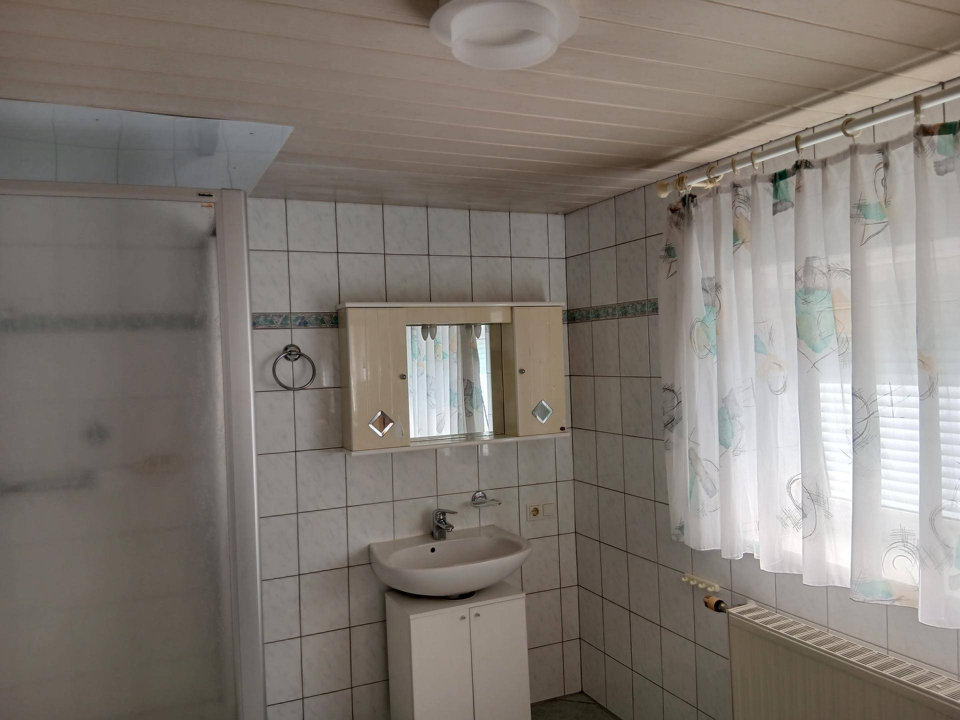 Waschbecken mit Spiegelschrank und Fenster im Badezimmer.