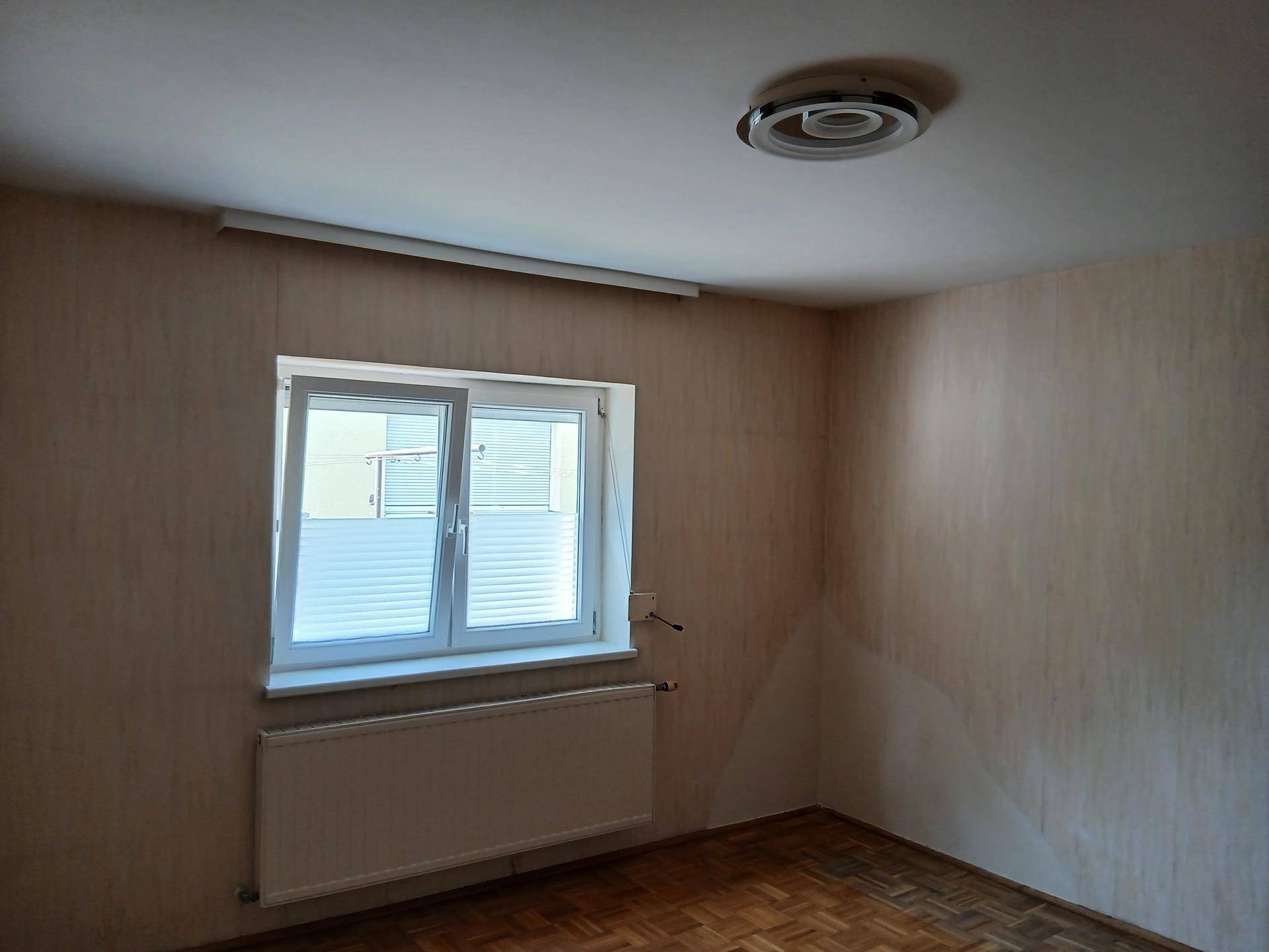 Helles Schlafzimmer mit Parkettboden, Fenster und Heizkörper.