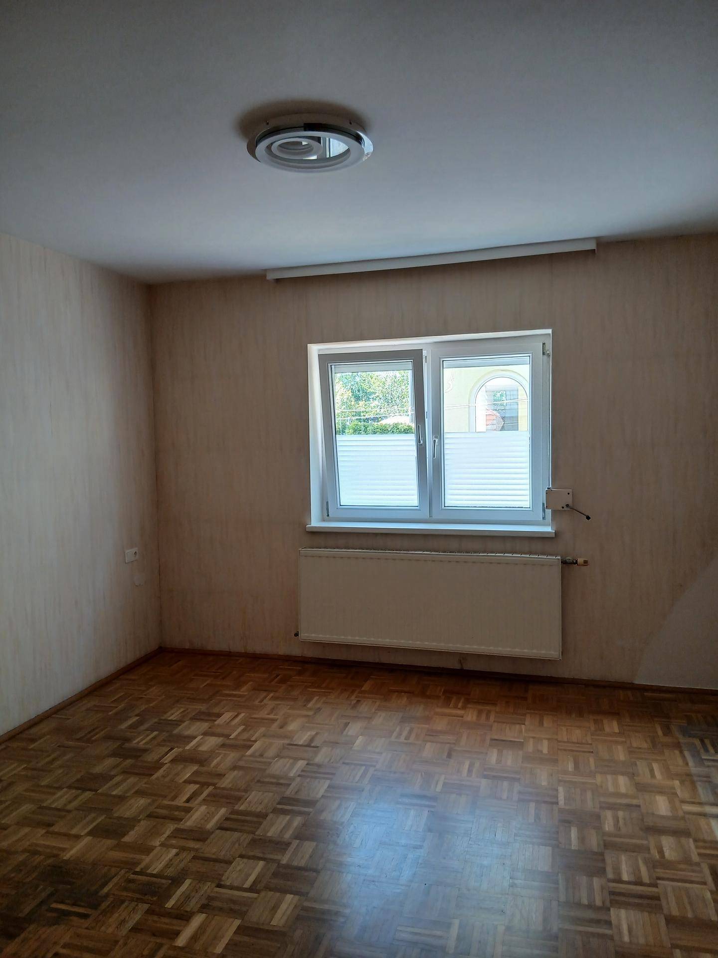 Leeres Schlafzimmer mit Parkettboden, Fenster und Heizkörper, bereit zur Einrichtung.