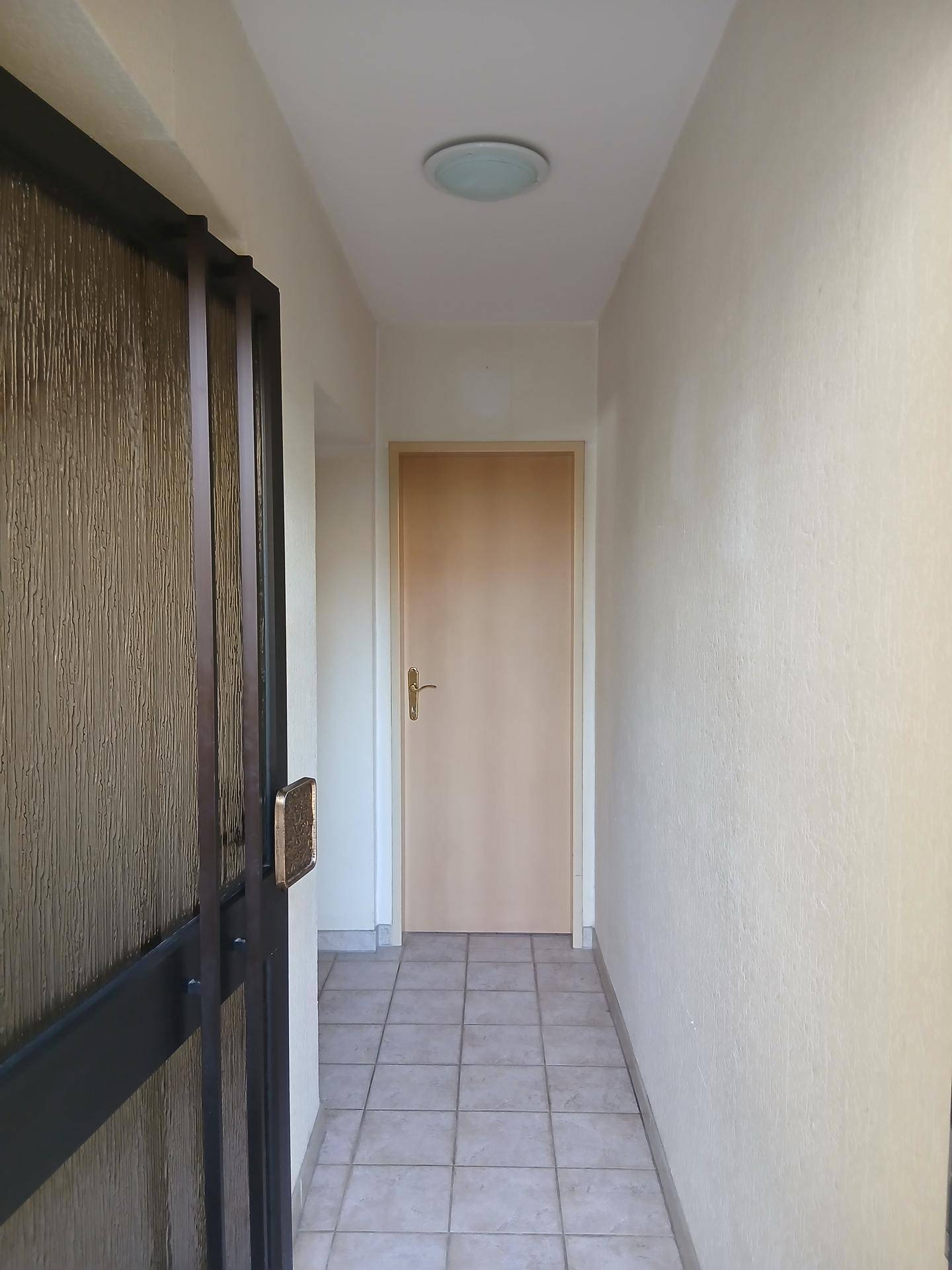 Heller Flur mit Fliesenboden und Holztür, der zu weiteren Räumen führt.