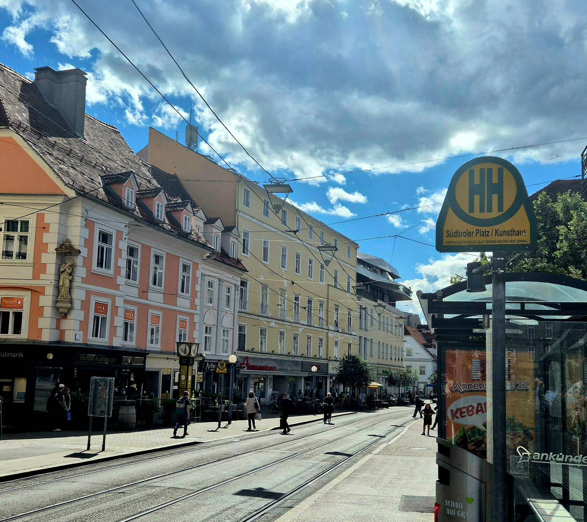 Stadtansicht mit Straßenbahn, historischen Gebäuden und einer Haltestelle.