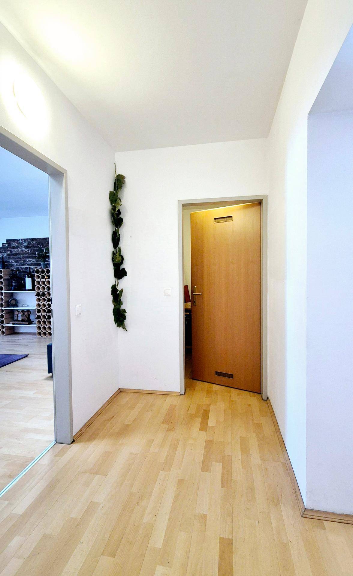 Heller Flur mit Holzboden und einer Holztür, die zu einem anderen Raum führt.