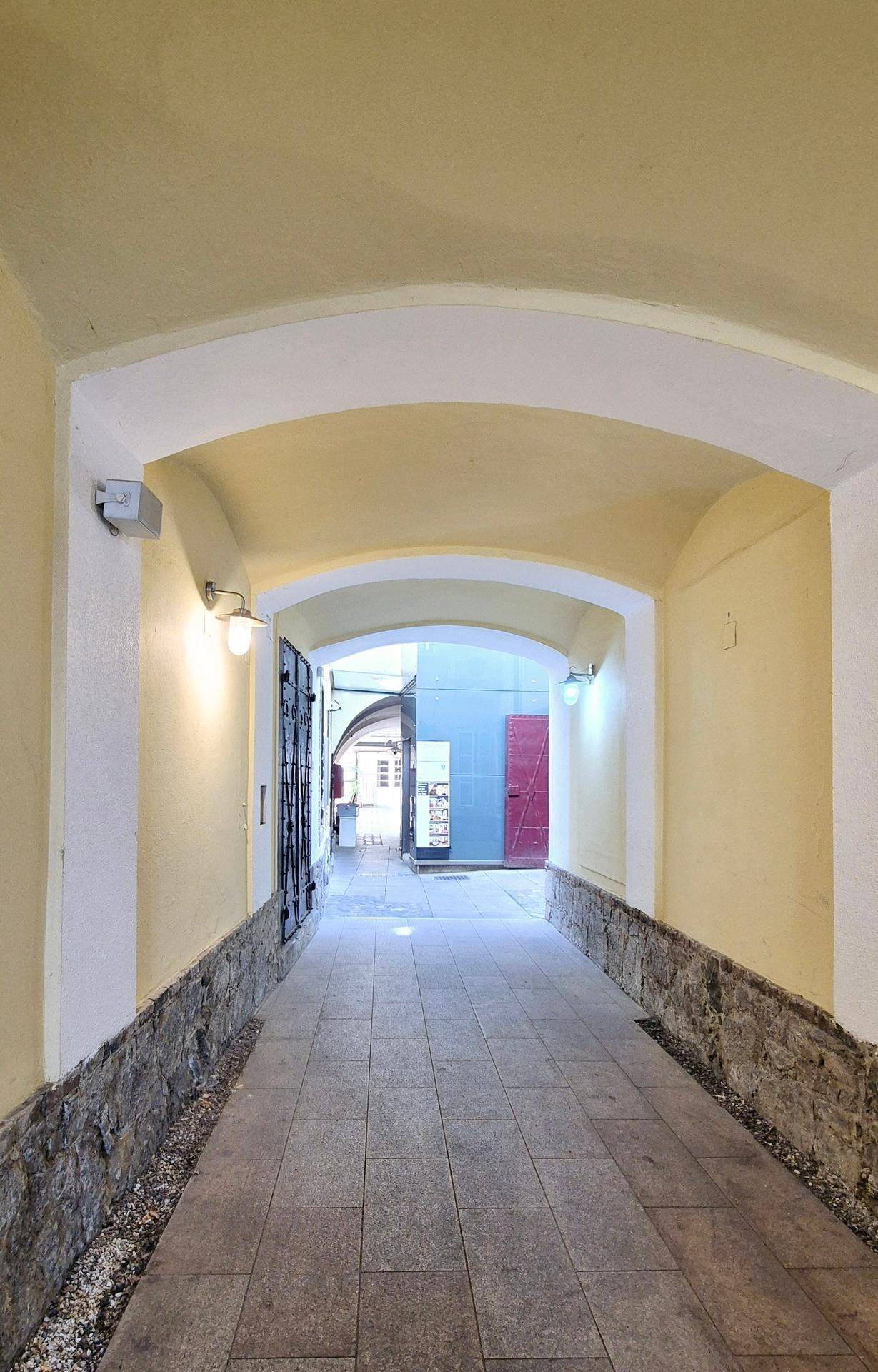 Überdachter Durchgang mit Steinmauern und Fliesenboden, der zu einem Innenhof führt.