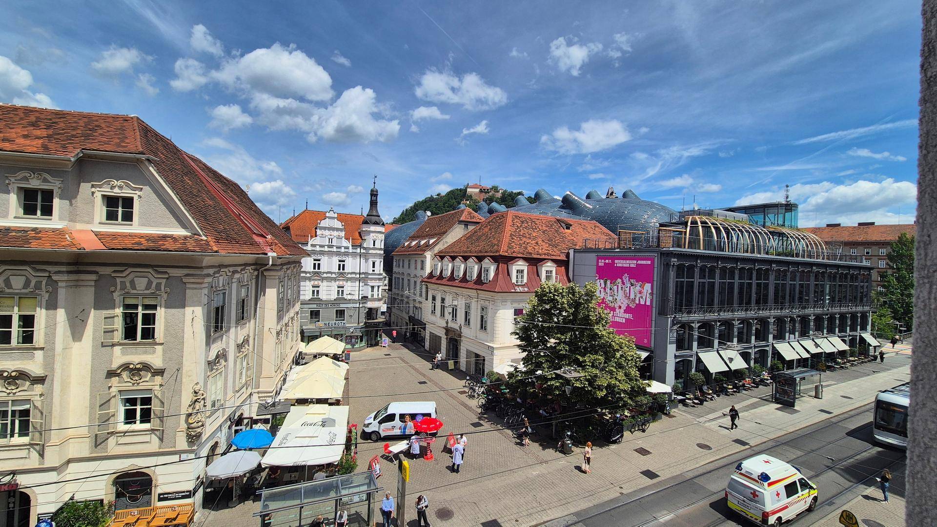 Panoramablick auf eine belebte Stadtstraße mit historischen Gebäuden und modernem Kunsthaus.