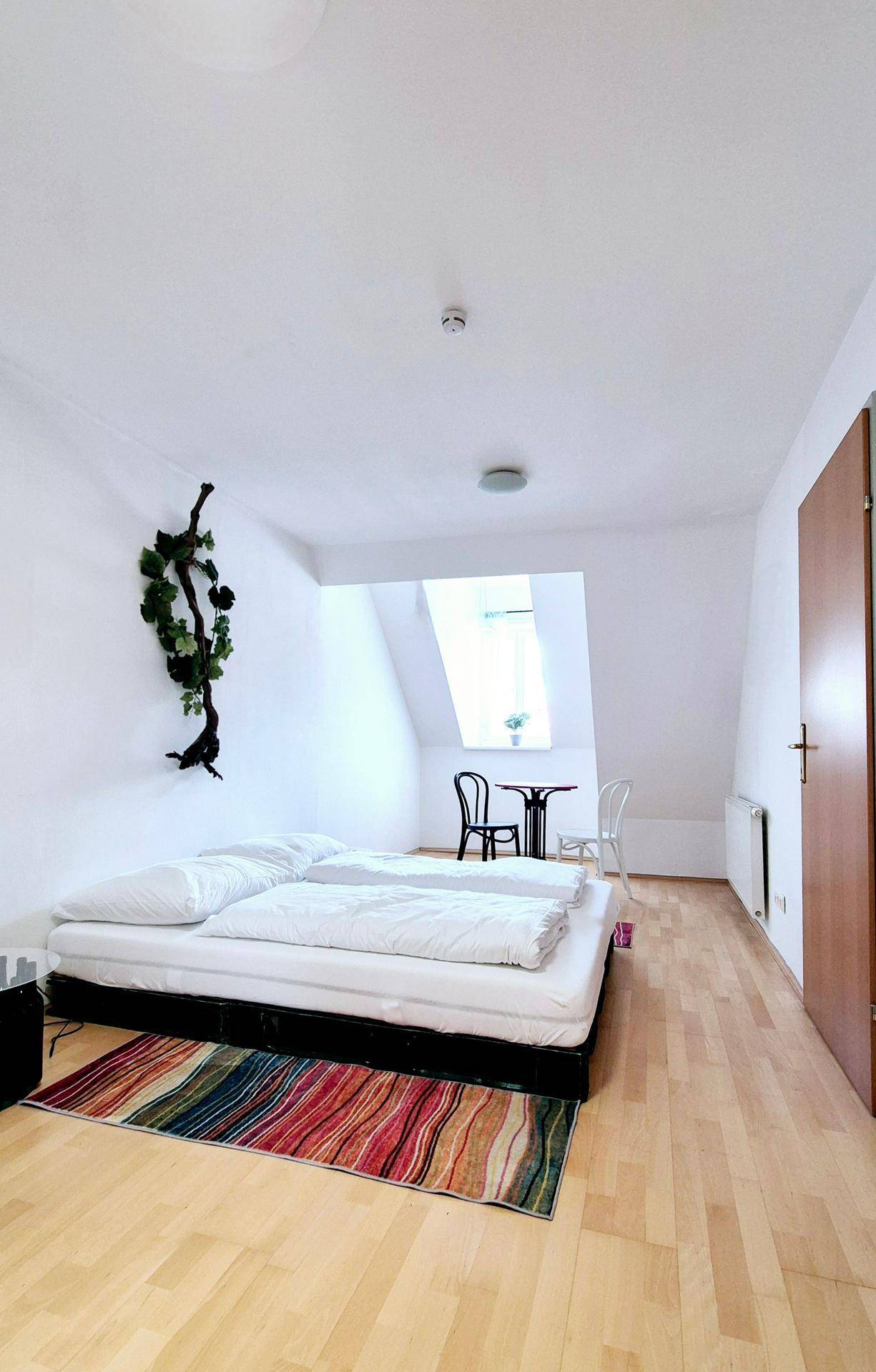 Schlafzimmer im Dachgeschoss mit Holzboden, Bett und farbenfrohem Teppich.