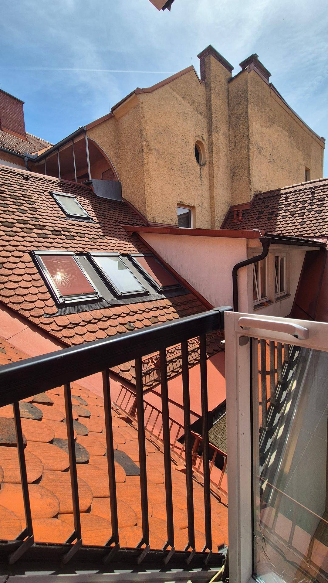 Blick von einem Balkon auf die Dächer der Stadt mit Dachfenstern und historischer Architektur.
