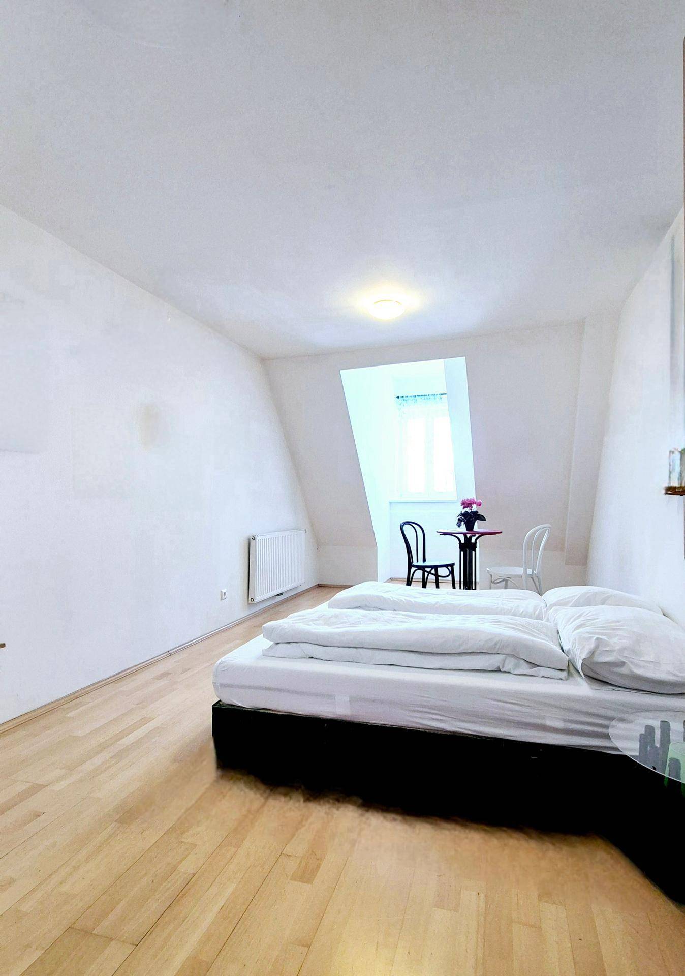 Helles Schlafzimmer im Dachgeschoss mit Holzboden, einem Bett und einem kleinen Tisch.
