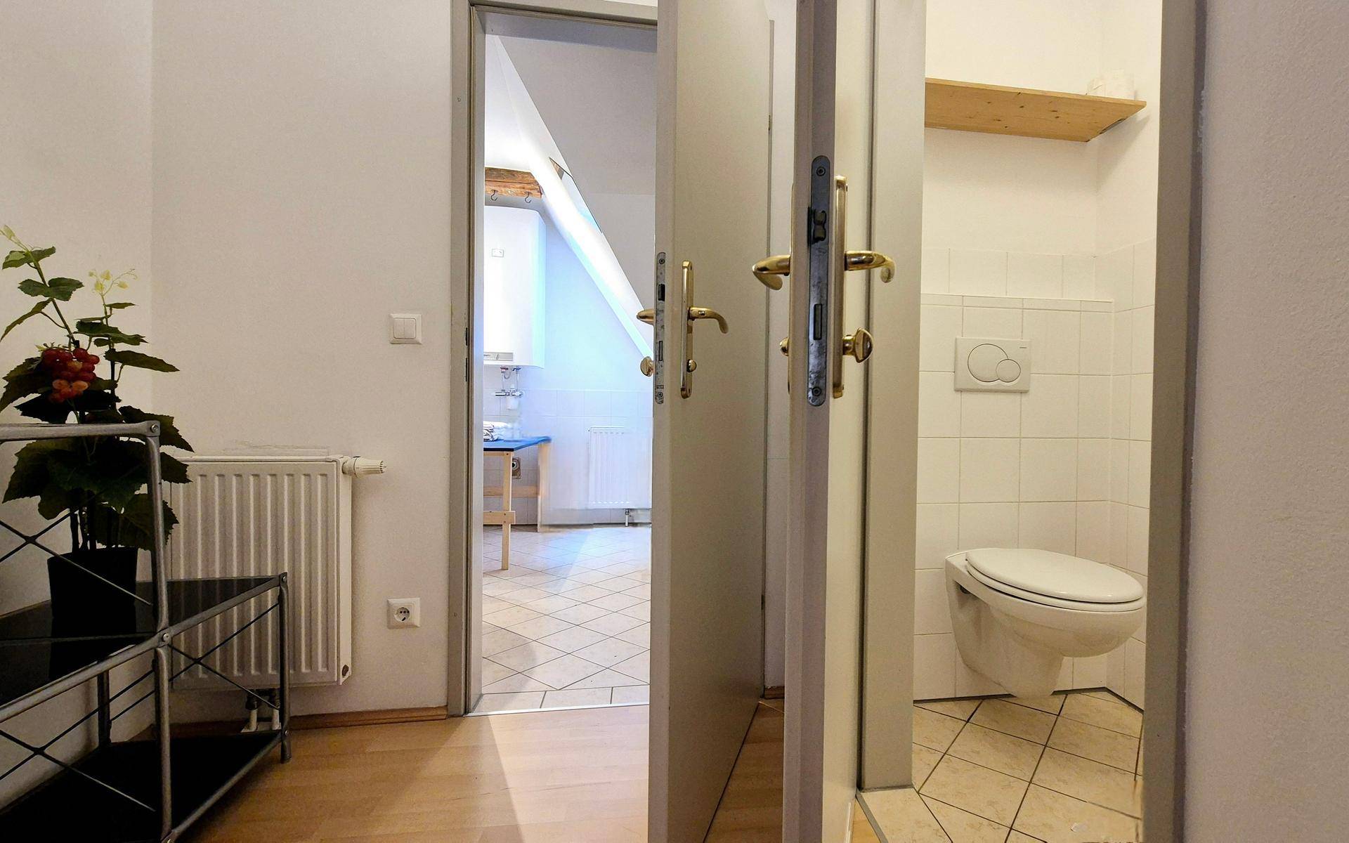 Flur mit Zugang zu einem WC und Blick in einen weiteren Raum.