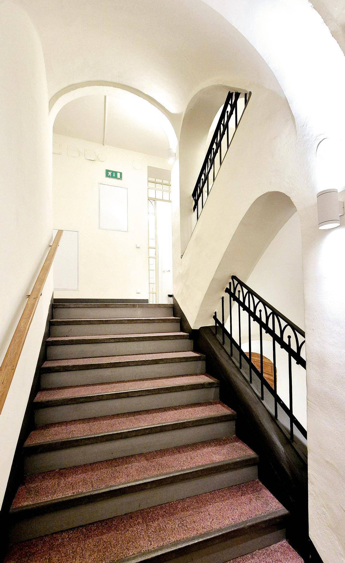 Historisches Treppenhaus mit gewölbten Decken, schmiedeeisernem Geländer und Teppichstufen.